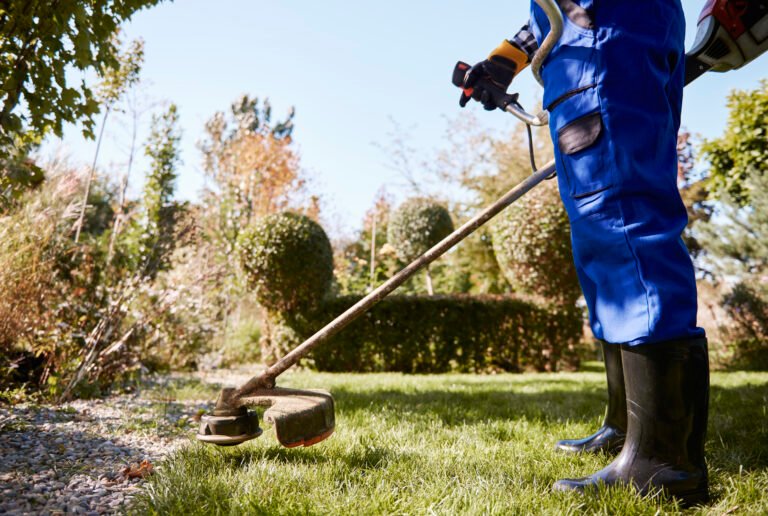 gardener with weedwacker cutting the grass in the garden